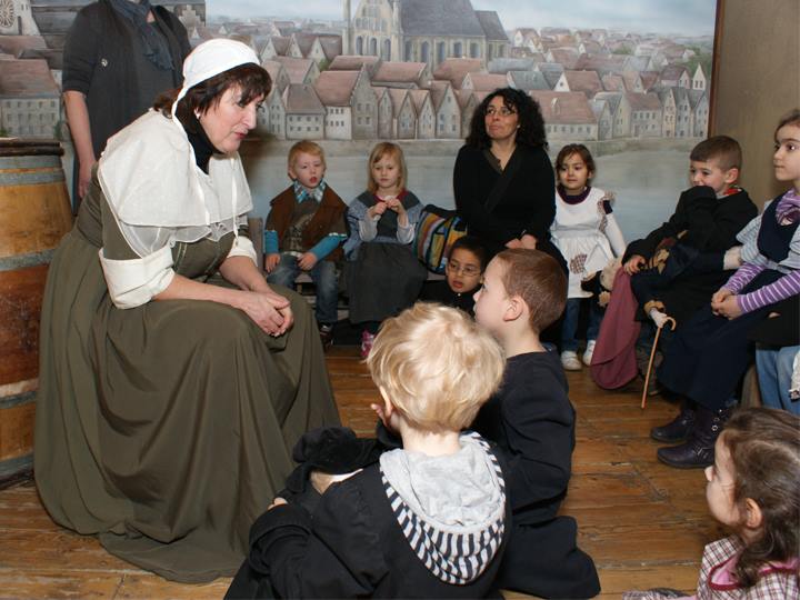 Children dressed in historical costumes participate in an interactive tour at the Bremen Story House. They are surrounded by period decor and props, creating an immersive historical experience.