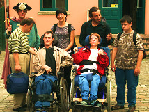 A group of people with disabilities, including two individuals in wheelchairs, in front of the entrance to the Bremen Story House. They are accompanied by a caregiver and an employee in historical costume. The historic facade of the building can be seen in the background.